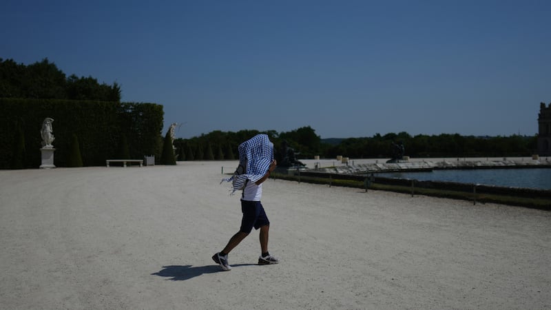 Un hombre se protege del sol mientras camina por el jardín del Palacio de Versalles, a las...